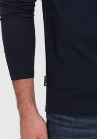 Dunkelblaues Langarm-T-Shirt aus Baumwolle, mit enger Passform, rundem Ausschnitt und einem kleinen Markenschild am Saum.