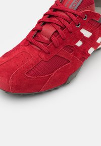 Scarpa sportiva rossa con tomaia in suede e mesh, lacci piatti e dettagli bianchi. La punta presenta piccole perforazioni per la ventilazione.