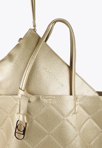 Dwie złote torebki nałożone na siebie, prezentujące skórę o fakturze. Większa torba ma diamentowy wzór, podczas gdy mniejsza jest gładka z logo.