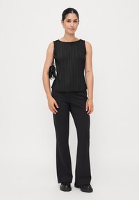 Haut noir plissé sans manches avec un col rond, associé à un pantalon évasé noir taille haute et des chaussures à plateforme noires. Finition texturée.