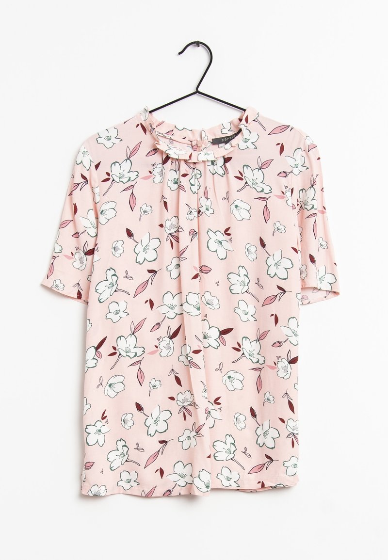 Blouse rose à manches courtes avec motif floral blanc et bordeaux, col à volants, suspendue à un cintre noir sur fond blanc.