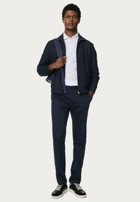 Chaqueta con cremallera de color marino sobre una camiseta polo blanca, combinada con pantalones marinos y zapatillas negras. Presenta una textura suave y un diseño sencillo.