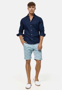 Navy button-down shirt, light blue shorts with palm tree print, white slip-on shoes, relaxed fit, smooth fabric, casual summer outfit.