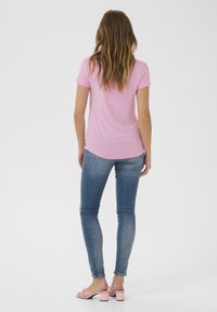 Roosa lühikeste varrukatega T-särk ümarate servadega, koos sobivate siniste teksadega. Model kannab heledat roosa kontsaga sandaali.