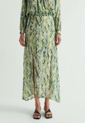 Mujer que lleva una falda larga con abertura y un top a juego con patrones abstractos en verde, azul y beige, combinados con tacones negros abiertos.