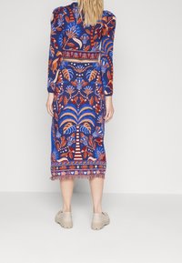 Robe à manches longues en bleu avec des motifs floraux et de palmiers vifs en rouge et orange. Dotée d'un ourlet à franges et d'une silhouette ajustée.