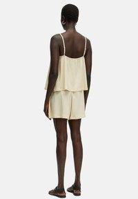 Lichtbeige twee-delig outfit met een gelaagde tanktop met dunne bandjes en bijpassende shorts. Zachte textuur, losse pasvorm en minimaal ontwerp.