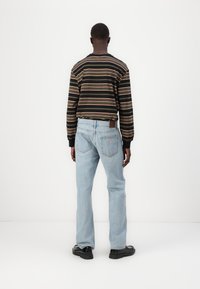 Camisa de manga larga a rayas negras con rayas de varios colores; jeans de mezclilla de color azul claro; calzado negro; etiqueta de marca visible en los jeans.