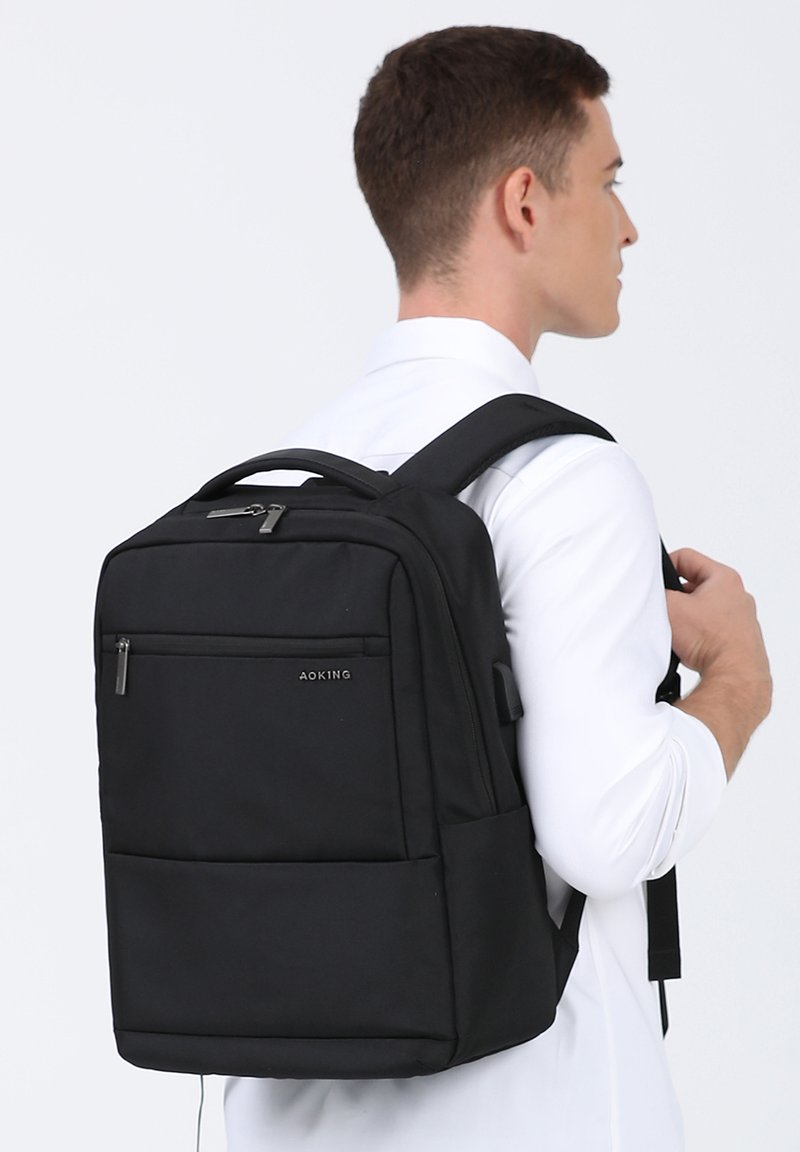 Zwarte stoffen rugzak met meerdere ritscompartimenten, rechthoekige vorm, gevoerde schouderbanden en een handvat aan de bovenkant. Logo op het voorpaneel.