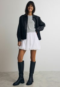 Jachetă din piele neagră, tricou gri, fustă albă pufosă și cizme negre până la genunchi cu toc gros. O ținută simplă și casual cu texturi variate.