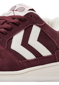 Burgunderfarbene Wildledersneaker mit weißen synthetischen Akzenten, ausgestattet mit einer strukturierten Oberfläche, einem auffälligen Logo und kontrastierenden Nähdetails.