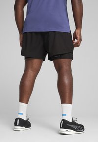 Sorte sportsshorts med sidelæg, parret med en lilla skjorte og sorte løbesko. Hvide sokker har et blåt logo.