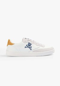 Witte leren sneakers met een blauw doodskop en botten logo, grijze suède accenten en een gele hieltab met een textuur witte zool.