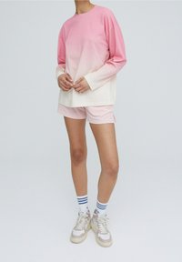 Rento asu, jossa on vaaleanpunaisesta kermaan liukuvärjätty pitkähihaisen paita, samansävyiset vaaleanpunaiset shortsit ja vaaleat lenkkarit raidallisilla sukilla.