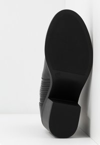 Czarny but z gładką cholewką i żłobieniami po bokach. Płaska gumowa podeszwa z teksturowanym gripem. Rozmiar oznaczony jako 37.