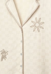 Cămașă albă din in cu un model texturat, având broderie cu un design floral și de palmier, și accente gri contrastante cusute pe guler.