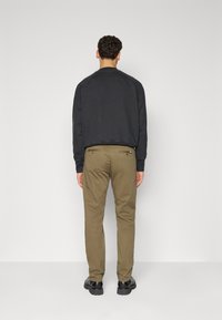Men's dark gray sweatshirt with a rounded neckline, paired with olive green chinos featuring back pockets and red button accents.