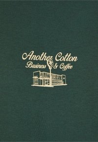 Dark green cotton fabric featuring a printed design of a building with "Another Cotton Business & Coffee" in cream color.