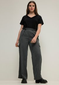 Musta V-päällyspaita yhdistettynä korkeavyötäröisiin, leveälahkeisiin, teksturoituihin harmaisiin housuihin, joissa on sivutaskut ja nyörivyö. Asusteena mustat kengät.