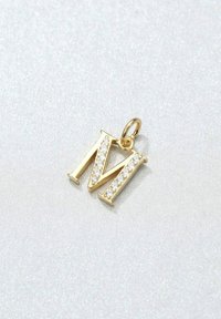 Goldener Buchstabe "M" Anhänger mit klaren Strasssteinen an einer Seite. Verfügt über eine kleine Schlaufe zur Befestigung. Glatte metallische Oberfläche.