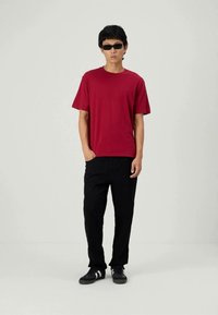 Camiseta de algodón roja, de mangas cortas, combinada con pantalones negros y zapatos negros. Los accesorios incluyen gafas de sol oscuras. Atuendo simple y casual.