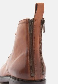 Botines de cuero marrón con cremalleras laterales dobles, puntera redondeada y una textura suave, con una lengüeta en el talón para facilitar su uso.
