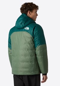 Groene en teal pufferjack met een capuchon, voorzien van een logo op de bovenrug, en een gladde, licht glanzende textuur.