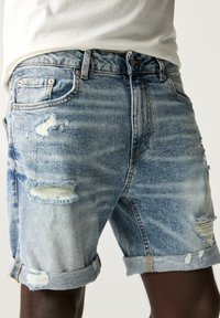 Light blue denim shorts with distressed details, rolled cuffs, and a classic five-pocket design. Features frayed edges and fading.