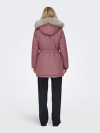 Parka imbottito rosa con cappuccio in pelliccia sintetica, vita con coulisse e polsini a costine. Indossato con pantaloni neri, visto da dietro. Tessuto liscio.