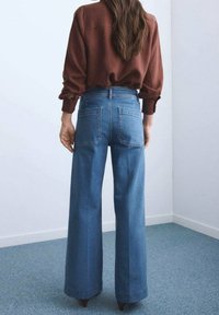 Jean en denim bleu taille haute avec jambes larges. Comprend un design classique à cinq poches et un tissu texturé.