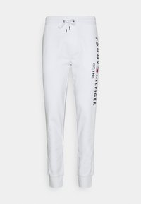 Vita sweatpants med elastisk midjeband och snörning. Har en vertikal "TOMMY HILFIGER"-logotyp och "EST. 1985" i blått på sidan.