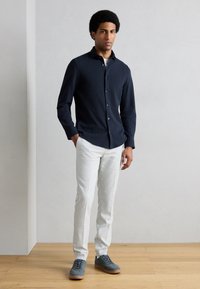 Granatowa koszula z długim rękawem i guzikami, białe dopasowane spodnie oraz szaro-niebieskie sneakersy z gumową podeszwą, na jasnoszarym tle.