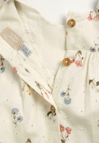 Blouse en coton floral crème, avec des fleurs brodées dans des teintes pastel, des boutons en bois et un design en œillets texturé.
