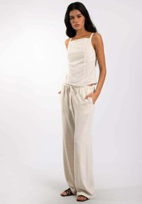 Top beige de lino con escote cuadrado y tirantes finos, combinado con pantalones beige sueltos que cuentan con una cinturilla elástica y bolsillos laterales.