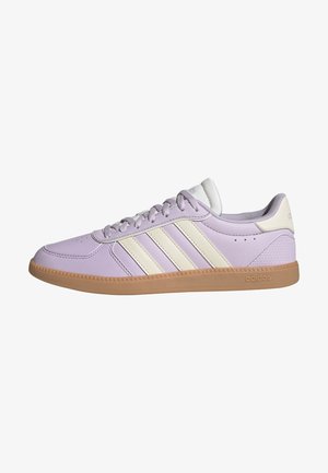 Fliederfarbener Adidas-Sneaker mit cremefarbenen drei Streifen, Gummisohle und Schnürsenkeln, von der Seite auf weißem Hintergrund gesehen.