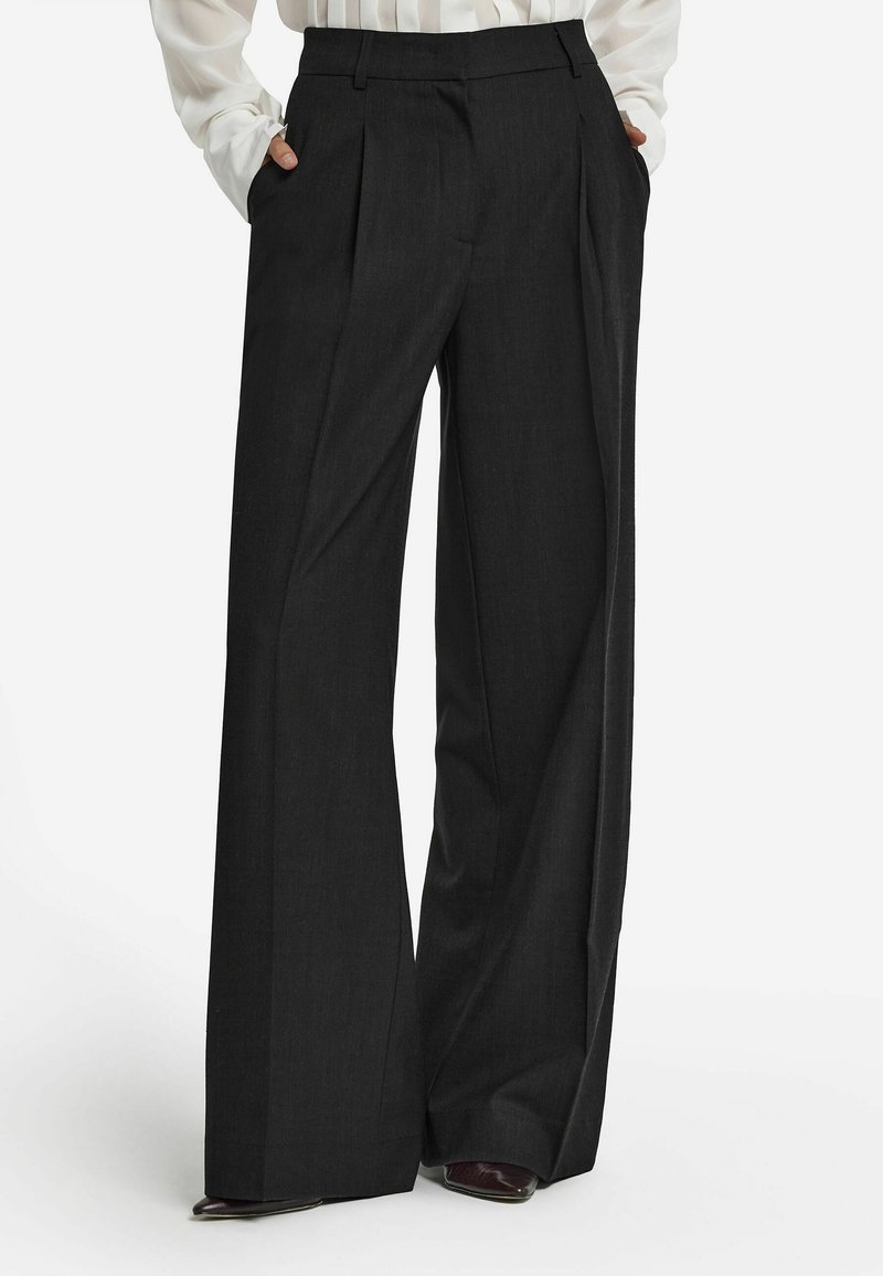 Svarta vida byxor i texturerat tyg. Har framfickor och veck, samt en skräddarsydd passform vid midjan.