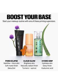 Three Milk Makeup primer products with ingredients: purple flowers by black tube, turmeric next to orange bottle, aloe leaf by green bottle.