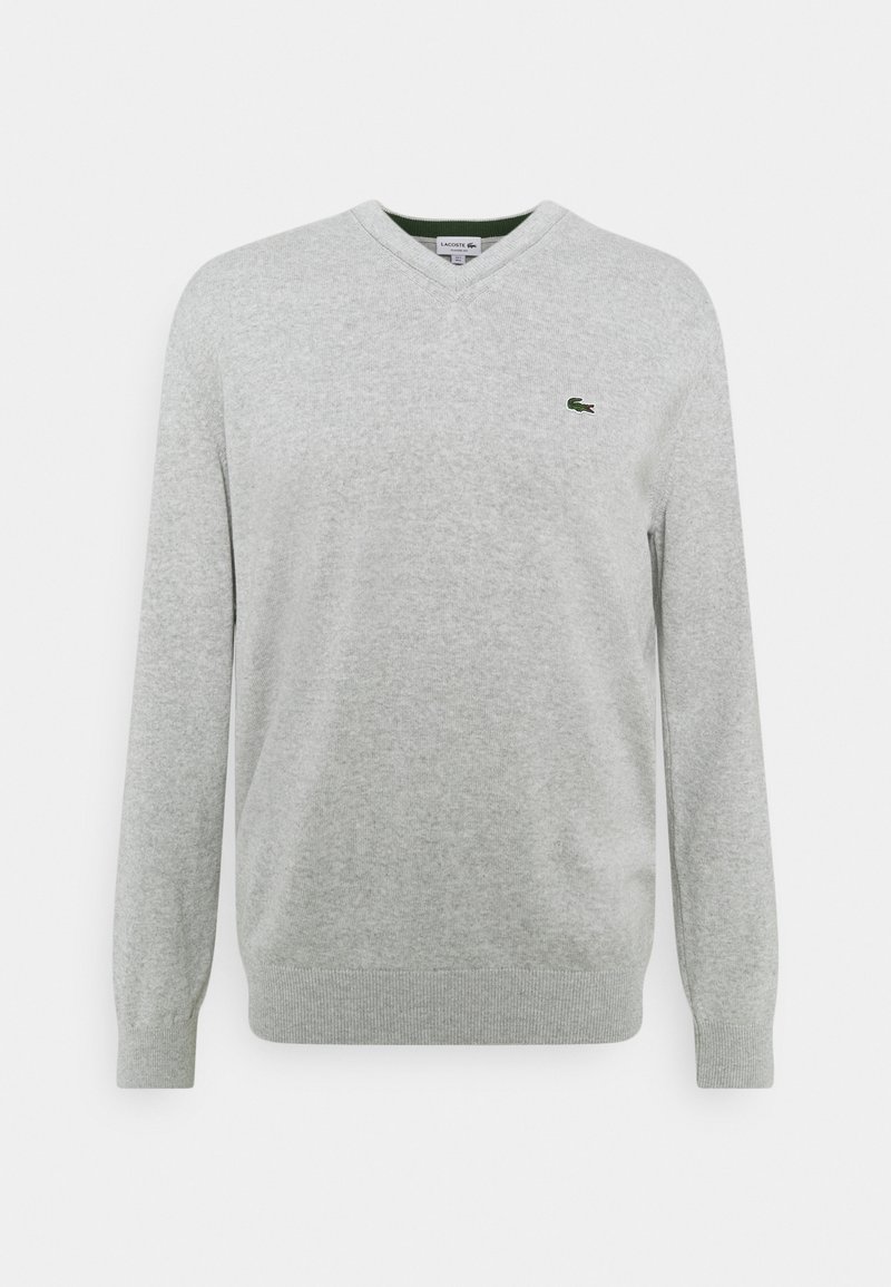 Pull gris en v en tissu doux, avec des manches longues et un petit logo vert sur la poitrine gauche. Ourlets et poignets côtelés.