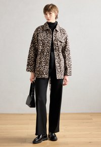 Veste en imprimé léopard avec une coupe décontractée, poche poitrine, fermeture à boutons, associée à un pantalon large noir et des chaussures noires brillantes.