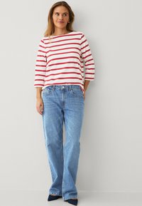 Top de manga larga a rayas rojas y blancas, combinado con pantalones de pierna ancha en un tono azul claro y zapatos de punta en azul oscuro. Tejido suave y ajuste relajado.