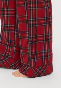 Rote karierte Loungehosen aus weichem Stoff, mit weitem Bein und kontrastierenden blauen und schwarzen Streifen im Muster, wobei ein barer Fuß sichtbar ist.