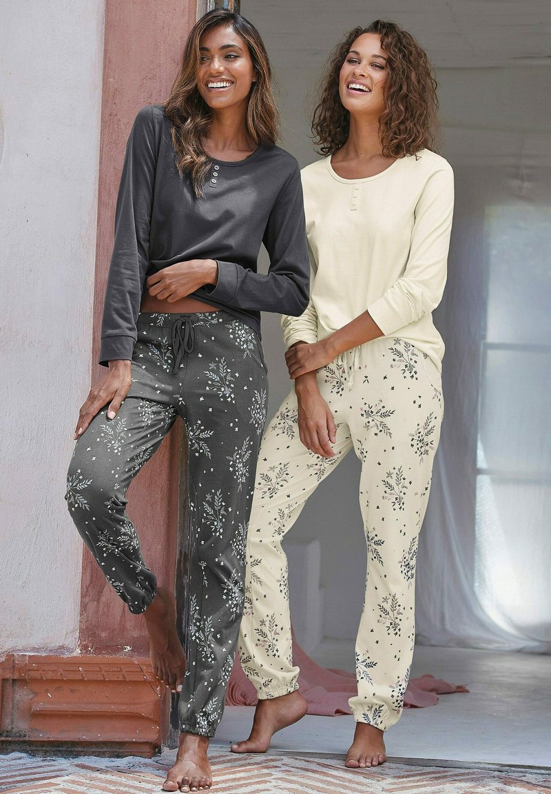 Two models wear long-sleeved tops and floral-patterned trousers. One top is dark gray, the other is light yellow. Trousers are gray and cream.