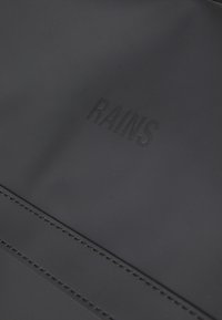 Black waterproof bag featuring a matte texture with the brand "RAINS" embossed on the surface. Minimalistic design with clean lines.