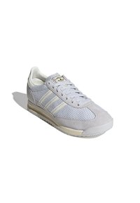 Light gray sneaker featuring a mesh upper, suede accents, white three-stripe design, and a textured rubber sole. Gold logo detail present.