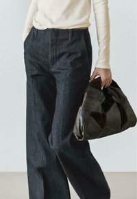 Pantaloni a gamba larga in denim scuro con vita alta, abbinati a una borsa in pelle scura e testurizzata con un design geometrico.