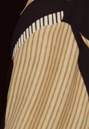 Close-up of beige fabric with diagonal brown stripes and a black section with vertical white stripes along the edge.