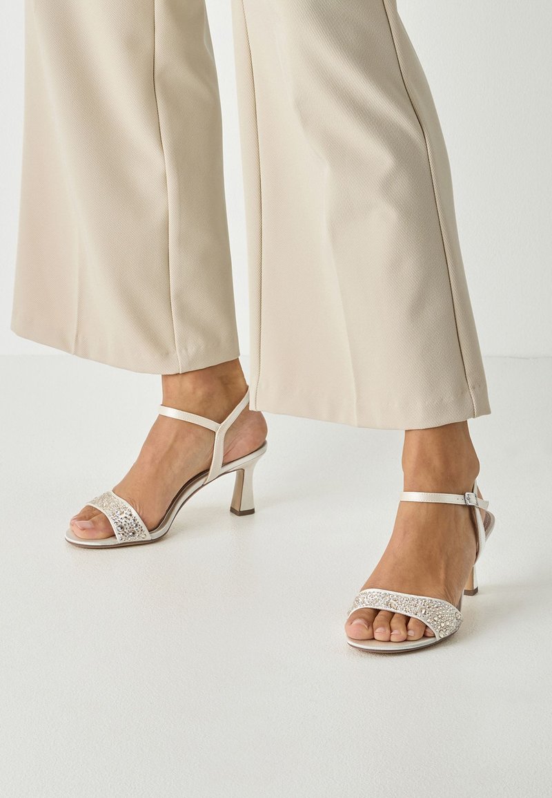 Μπεζ σανδάλια με τακούνι, με σχέδιο με λουριά, διακοσμητικό λουράκι στο μπροστινό μέρος και λεπτό λουράκι στον αστράγαλο. Διαθέτουν τακούνι τύπου block ύψους 5 εκατοστών για σταθερότητα.