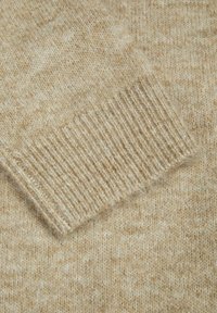Dettaglio di un maglione lavorato a maglia beige che mostra un bordo a coste con una consistenza morbida, che unisce fibre chiare e scure per un motivo sottile.