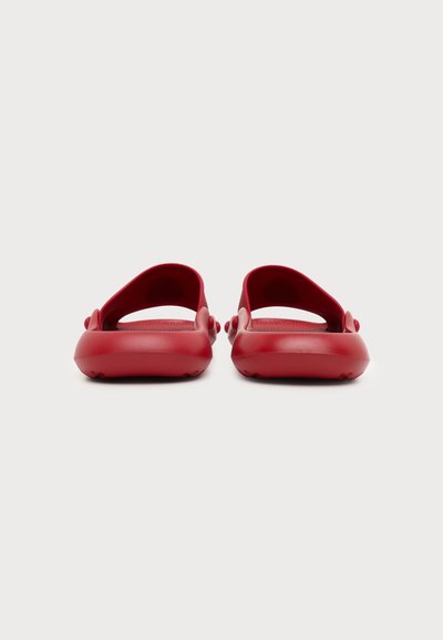 Paire de sandales en caoutchouc rouges à enfiler vues de dos sur un fond gris clair uni.