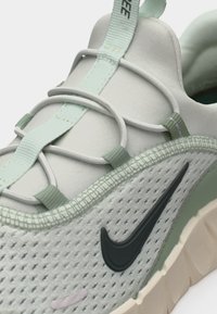 Ανοιχτό πράσινο και λευκό αθλητικό παπούτσι με μαύρο λογότυπο Nike, ελαστικά κορδόνια και επάνω μέρος από υφασμάτινο πλέγμα με υφή, απεικονιζόμενο από κοντινή γωνία.